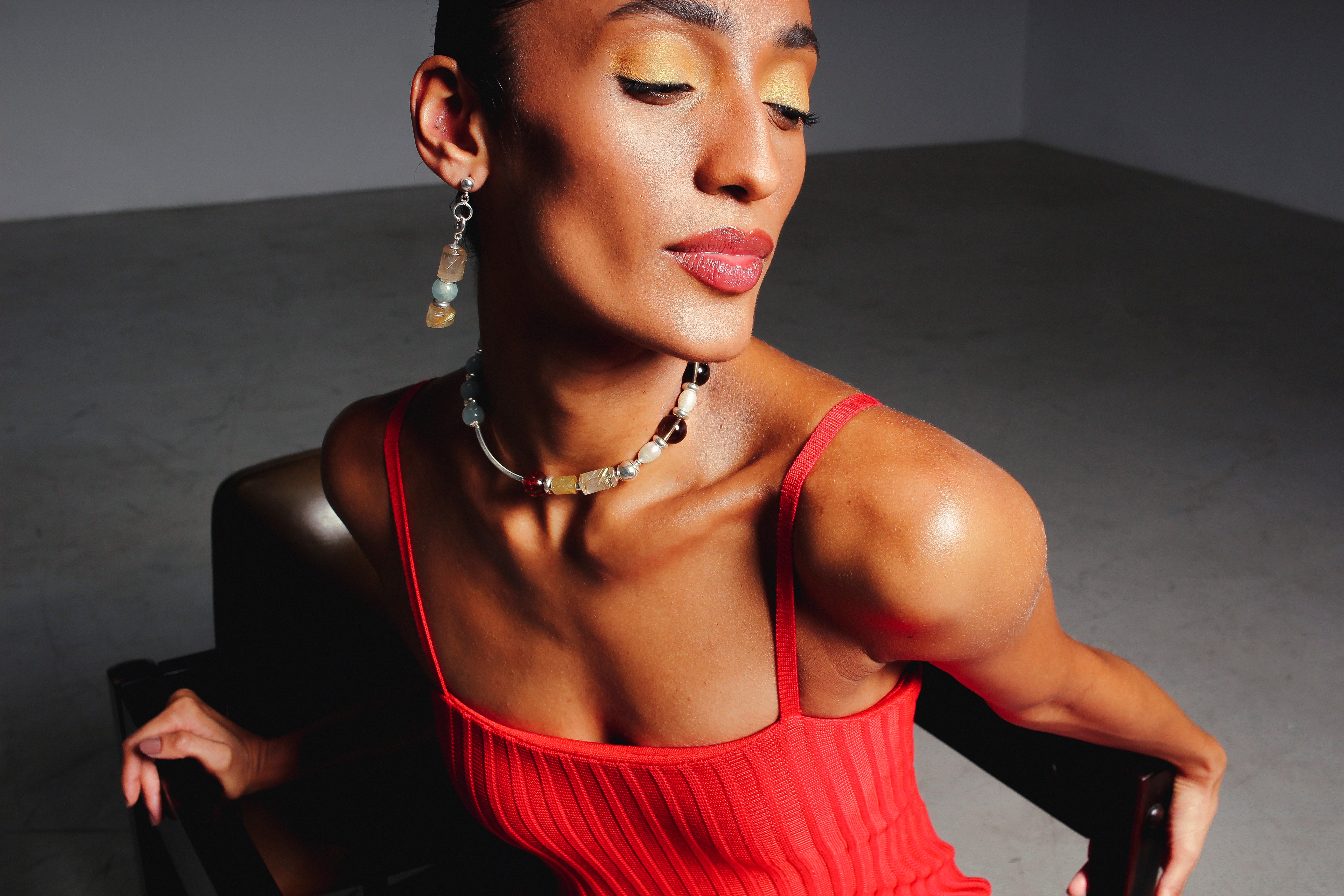 Modelo usando colar Tarsila A'IUNE com pedras naturais coloridas em look vermelho sofisticado.