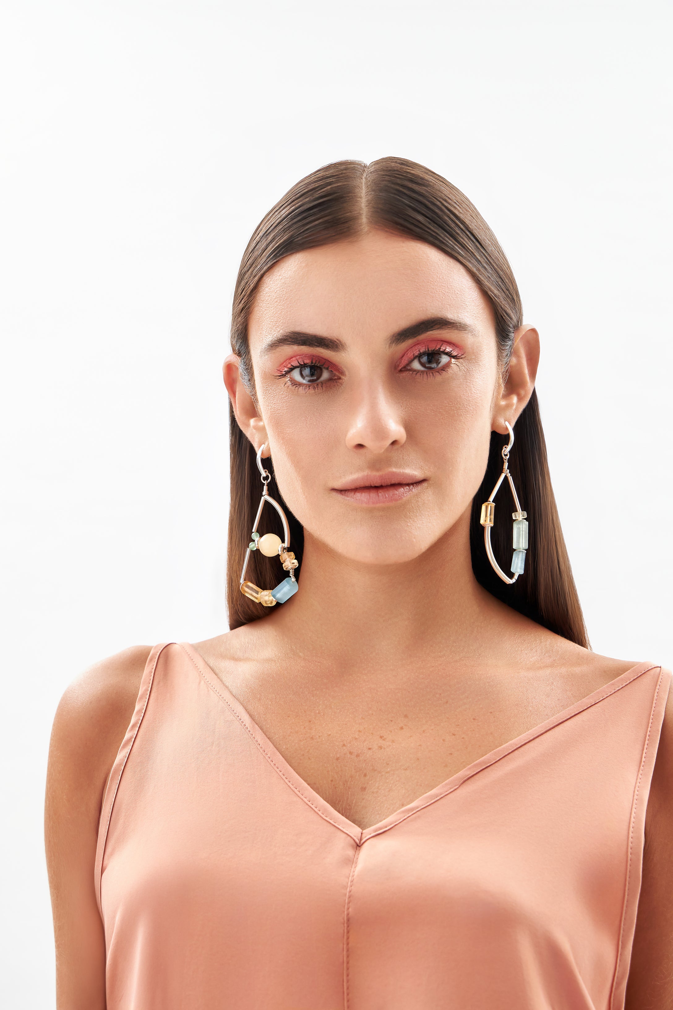 Modelo em foto frontal usando brincos Couture A'IUNE com pedras naturais coloridas e design assimétrico.